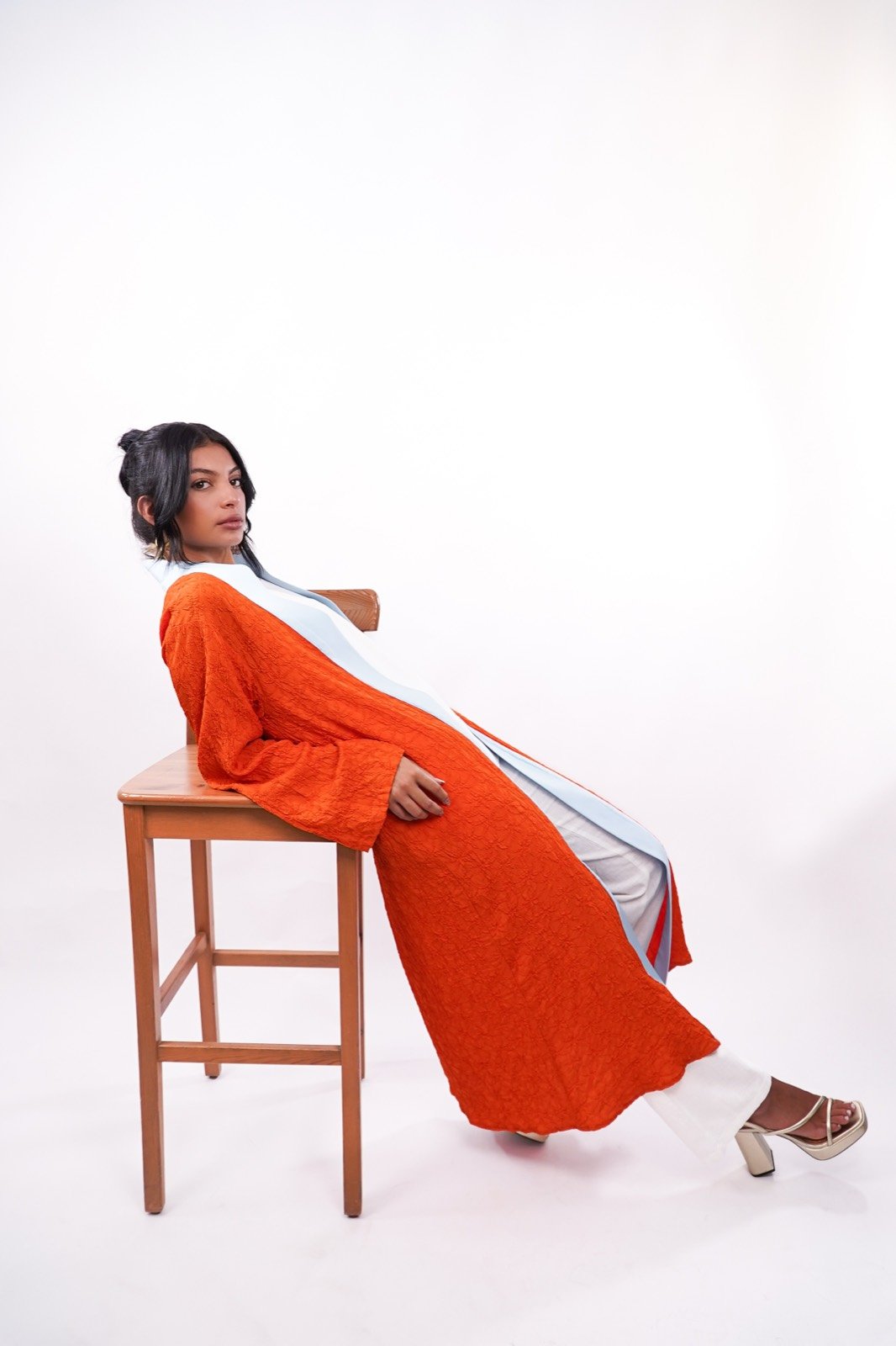 Amber Sky open-front robe in burnt orange, seated on a stool, full length, from the Le Kanz summer collection